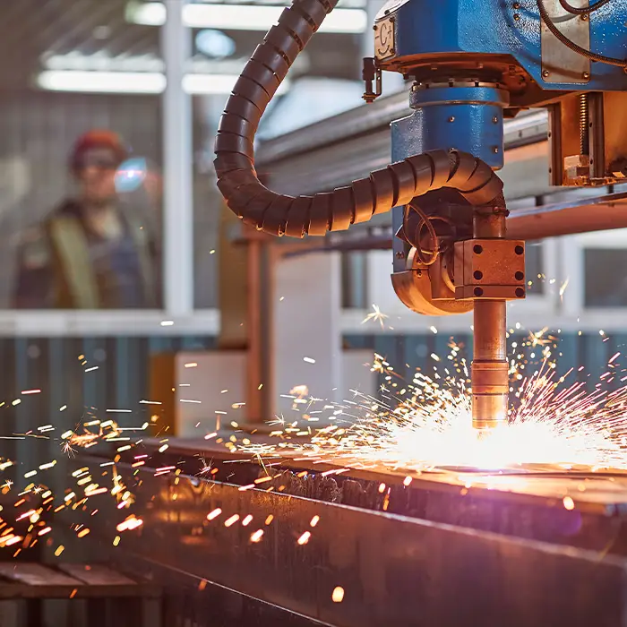A high-tech laser cutter creates sparks as it cuts metal. In the background, a worker watches.